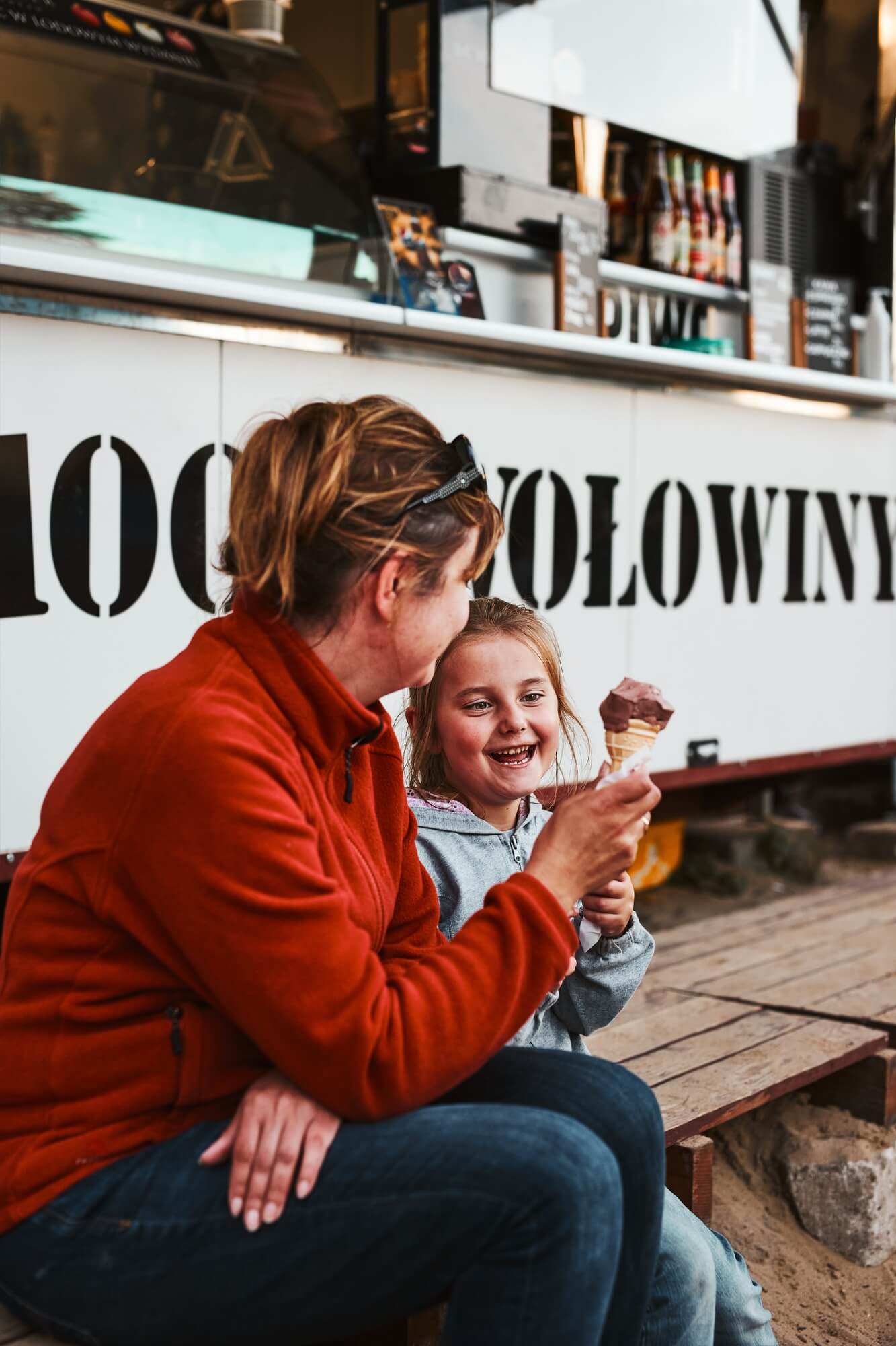 Mother and her daughter eating ice cream sitting on a step in front of food truck